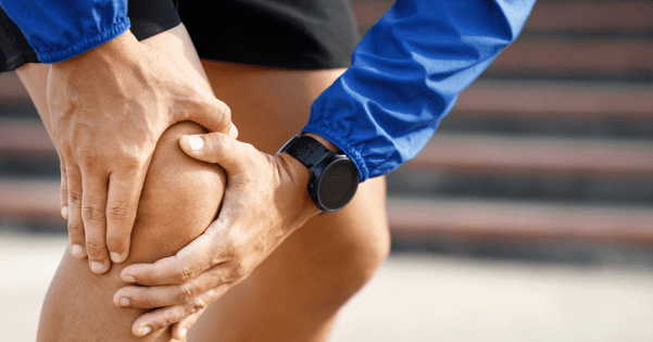 Close-up of an athlete in a blue jacket holding their painful knee.