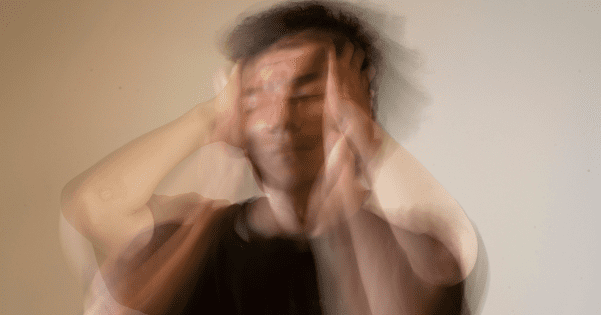 Motion-blurred photograph of a person holding their head in distress, depicting stress or disorientation.